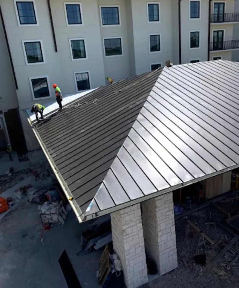 Crew installing standing seam metal roof panels on a commercial project in West Bend